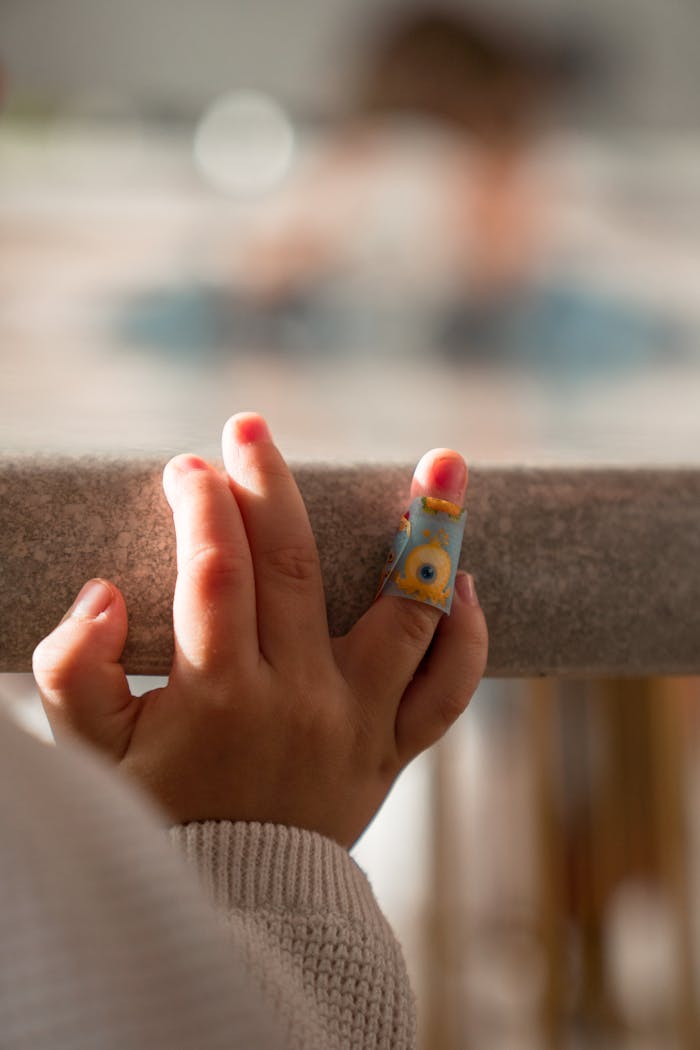 A close-up of a child's hand with a colorful bandage, resting on a poolside ledge.